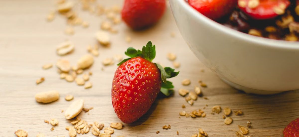 A close-up of a fresh strawberry breakfast bowl with granola on a wooden table, highlighting health and nutrition.